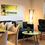 Wohn- und Essbereich mit Sofa, Stuhl und Tisch. Wandbild und Stehlampe sichtbar.