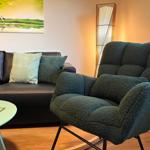 Ein dunkelgrüner Sessel steht neben einem Sofa mit Kissen. Eine Lampe und ein Bild an der Wand.