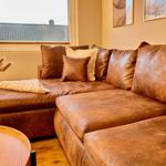 Ein braunes Ledersofa mit Kissen und einer Decke vor einem Fenster.