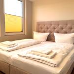 Schlafzimmer mit Doppelbett, Kopfteil und Fenster mit Jalousien.