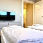 Zwei Betten mit weißen Laken, Fernseher und Tür zum Flur.