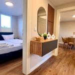 Schlafzimmer mit Bett und Fenstern. Flur mit Wandregal und Spiegel. Esszimmer mit Tisch und Stühlen.