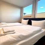 Schlafzimmer mit Doppelbett, weißen Laken und großen Fenstern.