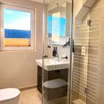 Badezimmer mit Dusche, Waschbecken und Toilette. Fenster mit Blick auf Dach.