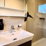 Bad mit Waschbecken, Spiegel und Dusche. Haartrockner und Seifenspender vorhanden.