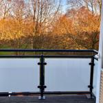 Terrasse mit Glasgeländer und Blick auf einen Wald mit kahlen Bäumen.