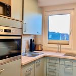 Küche mit Dunstabzug, Herd, Spüle und Fensterblick auf Dächer.