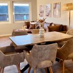 Essbereich mit Holztisch und sechs Stühlen. Im Hintergrund ein Sofa und Fenster.