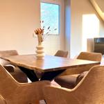 Esszimmer mit Holztisch, sechs Stühlen und Fenster. Fernseher im Hintergrund.