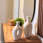 Holzkonsole mit zwei weißen Vasen, Pflanze und Holzschale. Spiegel und Holzpaneel an der Wand.