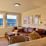 Wohnzimmer mit braunem Sofa, zwei Fenstern und drei Wandbildern.