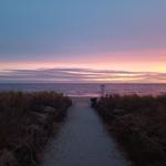 Sandweg führt zum Strand bei Sonnenuntergang mit rosa und blauem Himmel.