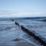 Wellen brechen an einem Holzpfahlzaun am Strand.
