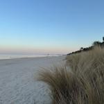 Weiterer Strand mit Dünen und Gras, Blick auf das Wasser und den Horizont.