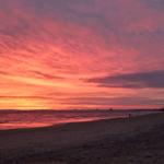 Strand bei Sonnenuntergang mit rosa-orange gefärbtem Himmel und Wellen.