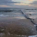 Strand mit Eis am Ufer und Steinen im Wasser bei Dämmerung.