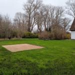 Grüner Garten mit Sandfläche neben einem weißen Haus mit Schieferdach.