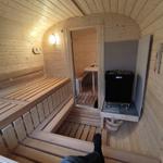 Sauna mit Holzbänken und Heizgerät. Durchgang zu einem weiteren Raum.