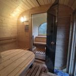 Sauna mit Holzbank und runder Sitzfläche. Durchgang zu weiterem Raum mit Fenster.