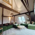 Wohnzimmer mit grünen Sofas, Holzbalken und Dachfenstern.
