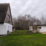 Haus mit Strohdach, grüner Rasen und kleiner Nebenstruktur im Hintergrund.