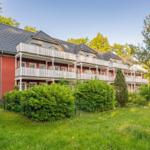 Rotes Mehrfamilienhaus mit weißen Balkonen und grüner Umgebung.