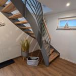Treppe mit Holzstufen und Metallgeländer. Fenster mit Segelschiffmodell. Pflanze und Wärmekörper an der Wand.