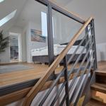 Treppenhaus mit Glasgeländer führt zu einem Schlafzimmer mit Dachschrägen und Holzboden.