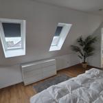 Schlafzimmer mit Dachfenstern, Bett, Schrank und Zimmerpflanze. Durchgang zur Waschküche.