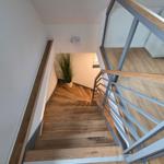 Holztreppe mit Metallgeländer führt zur oberen Etage. Pflanze und Licht an der Wand.