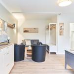 Wohnzimmer mit Sofa, zwei Sesseln und Fernseher. Anschlussraum mit Bett und Kleiderschrank.