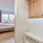 Schlafzimmer mit Bett, Fenster und Holzboden. Ankleidebereich mit Holzgarderobe und weißem Sitzbank.