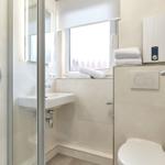 Badezimmer mit Dusche, Waschbecken und Toilette. Fenster mit Rollladen und Handtücher.