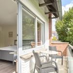 Schlafzimmer mit Balkon, Tisch und Stühlen. Blick auf grüne Bäume.