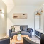 Ein Wohnzimmer mit grauem Sofa, Holztisch und Kleiderschrank mit Haken.