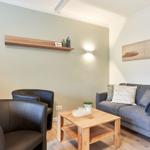 Ein Wohnzimmer mit grauem Sofa, zwei schwarzen Sesseln und einem Holztisch.