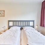 Zwei Betten mit weißen Bettwäsche, Nachttische und Lampen, Fenster mit lila Vorhang.