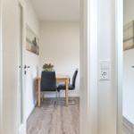 Essbereich mit Tisch, zwei Stühlen und Blumen. Wandbild und Holzboden.