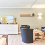 Wohnzimmer mit Sofa, zwei Sesseln, Couchtisch und Fernseher auf Schrank.