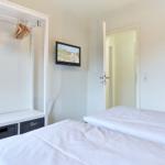 Zwei Betten, Kleiderschrank mit Haken und Wandfernseher in einem Schlafzimmer.