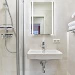 Badezimmer mit Dusche, Waschbecken und Spiegel mit Beleuchtung. Handtücher auf Regal.