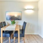 Esszimmer mit Holztisch, vier Stühlen, Wandbild und Bücherregal.