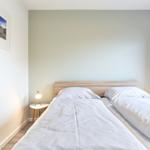 Zwei Einzelbetten mit weißen Bettwäsche, Nachttisch mit Lampe und lila Vorhänge.