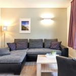 Wohnzimmer mit grauem Sofa, Holztisch und lila Vorhängen.