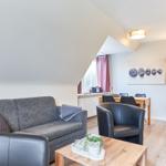Wohnzimmer mit Sofa, Sessel und Esstisch. Dachgeschoss mit Holzboden und Fenster.