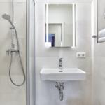 Badezimmer mit Dusche, Waschbecken und Spiegel mit Beleuchtung. Handtücher auf Regal.