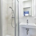 Badezimmer mit Dusche, Waschbecken und beleuchtetem Spiegel.