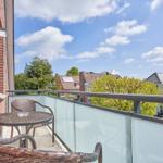 Balcony with wicker furniture and glass railing overlooking rooftops and trees.