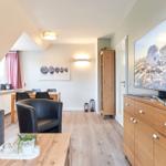 Wohnzimmer mit TV, Sofa, Sessel und Essbereich. Holzboden und große Fenster.