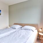 Ein Schlafzimmer mit Doppelbett, Nachttisch und Lampe. Wandbild und lila Vorhänge.